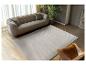 Salon moderne avec canapé beige, tapis ondulé et fauteuil en cuir.