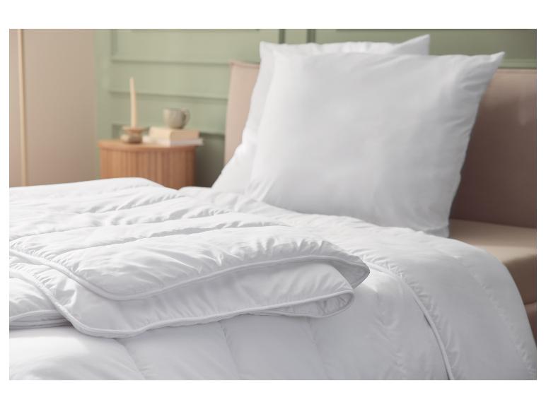 Couette et oreiller blancs sur un lit, avec un intérieur de chambre en arrière-plan.