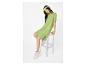 Femme en robe vert lime et baskets blanches, assise sur un tabouret transparent.
