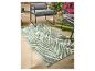 Tapis d'extérieur vert et blanc à motif de feuilles de palmier, entouré de mobilier de jardin et de plantes.