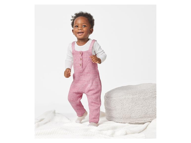 Un bambin dans un barboteuse en tricot rose joue sur une couverture blanche.