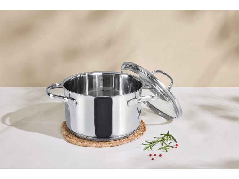 Casserole en acier inoxydable avec couvercle en verre et épices sur surface en marbre.