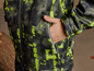 Une veste softshell verte et jaune avec une fermeture éclair et des poches.