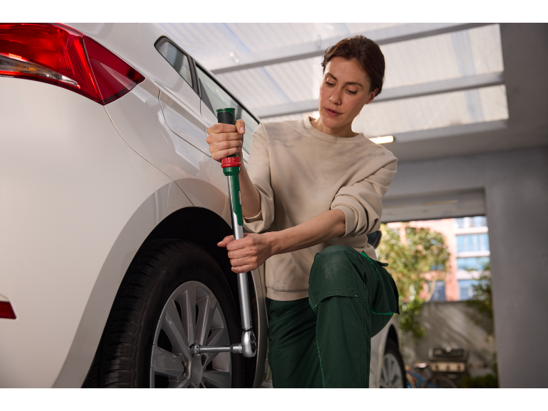 Femme changeant un pneu de voiture avec une clé en croix dans un garage.