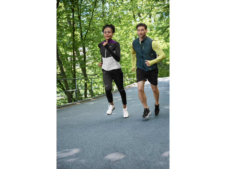 Deux coureurs en tenue de sport faisant du jogging en extérieur, femme en veste et homme en gilet.