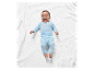 Un bébé heureux allongé sur une couverture blanche tricotée portant un pyjama bleu clair.