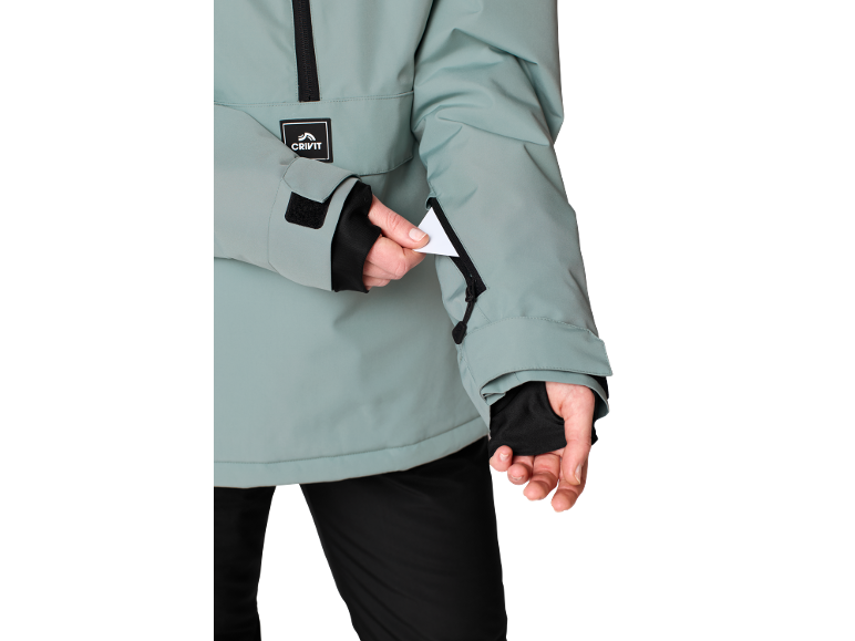 Personne en veste vert menthe avec fermeture éclair noire et étiquette blanche dans la poche de la manche.