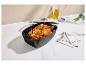 Poulet rôti dans un plat de cuisson noir avec légumes, huile et épices sur une surface en marbre blanc.