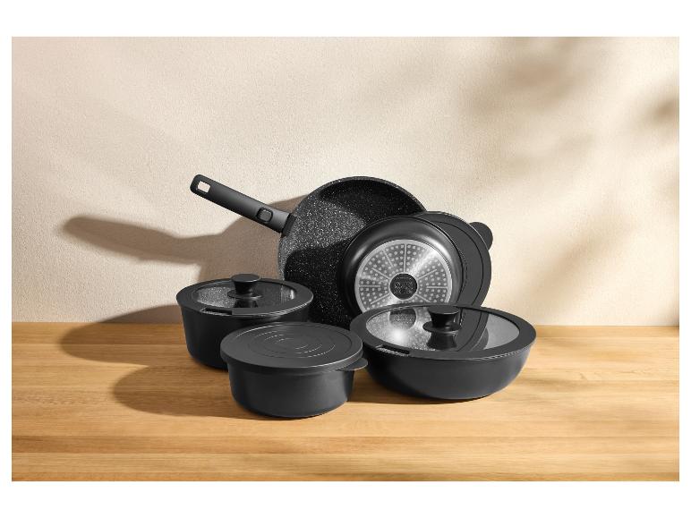 Ensemble d'ustensiles de cuisine noirs, dont une poêle, des casseroles et des couvercles, sur un comptoir en bois.