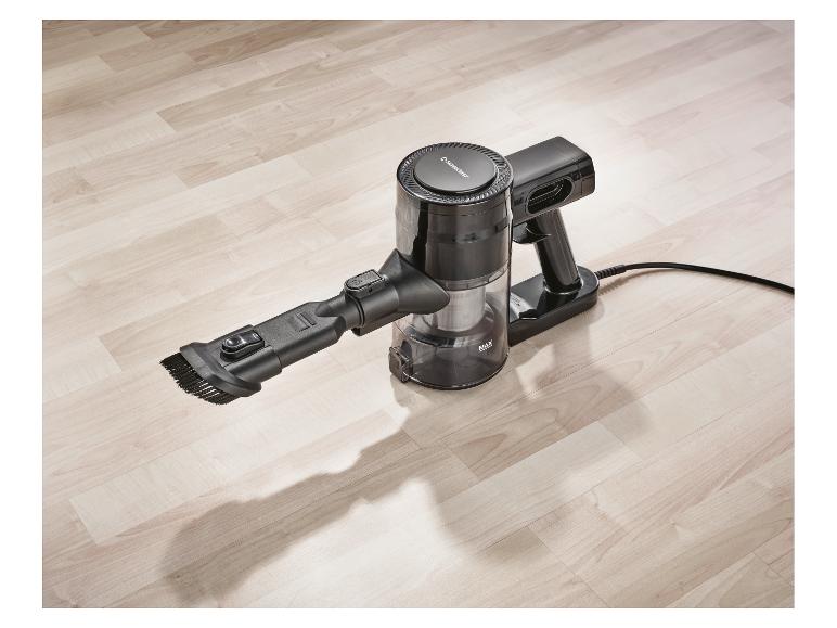 Aspirateur à main noir avec brosse sur un plancher en bois clair.