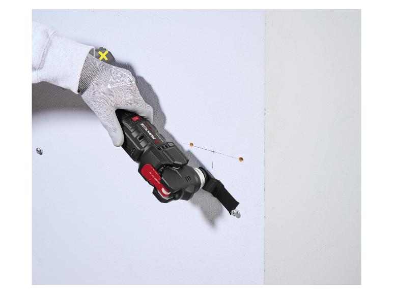 Main gantée utilisant un outil multifonction pour découper un mur.