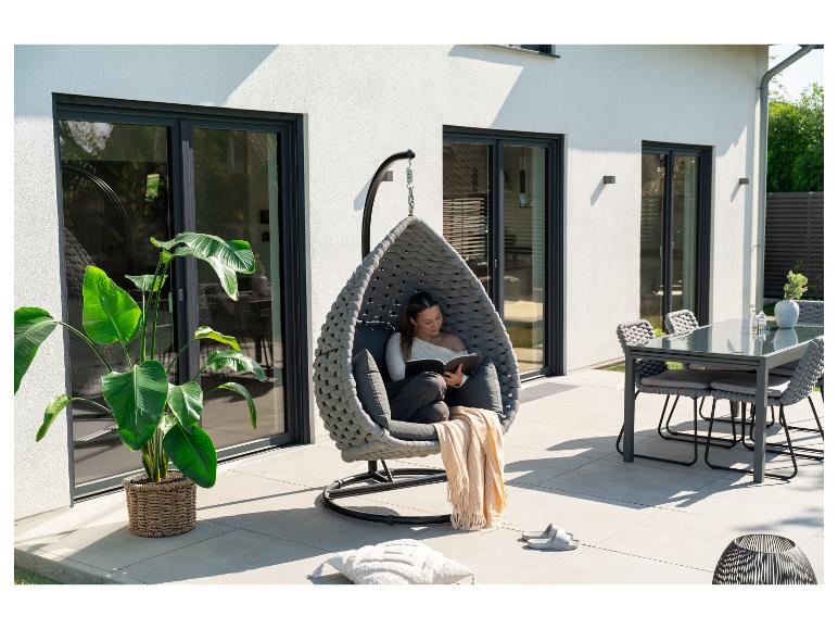 Femme lisant dans un fauteuil suspendu sur une terrasse avec table à manger et plantes.