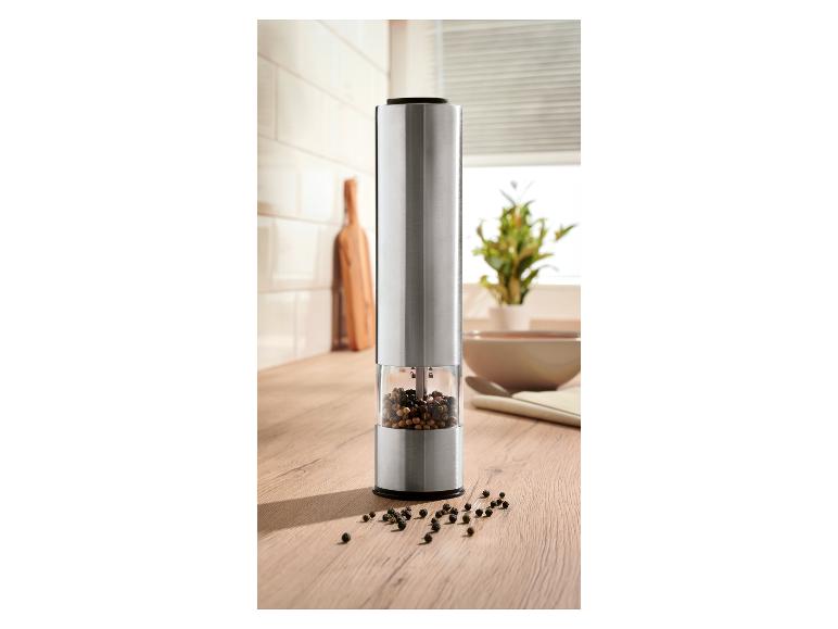 Moulin à poivre électrique en acier inoxydable avec grains de poivre visibles sur un comptoir de cuisine en bois.
