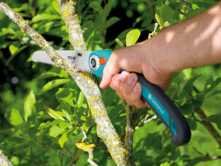 Une main utilisant une scie à élaguer Gardena pour couper une branche.