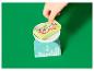 Une main d'enfant plaçant des cartes de jeu 'Candy Beans' sur une balance de cuisine.