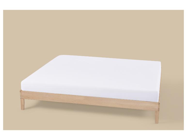 Un matelas blanc sur un sommier en bois clair, sur un fond beige.