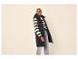 Femme en gilet long matelassé noir, pull rayé et jean, posant avec un sourire.