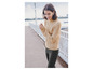 Une femme porte un pull beige en câble avec un pantalon noir.