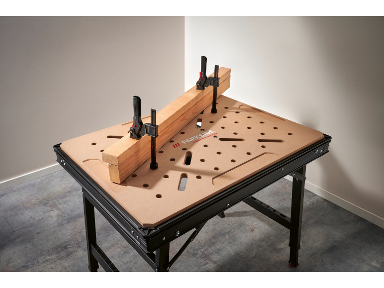 Établi avec plateau perforé et deux serre-joints maintenant une poutre en bois.