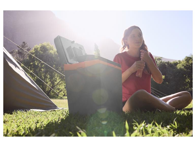 Femme en camping avec une glacière portable, buvant une boisson au soleil.