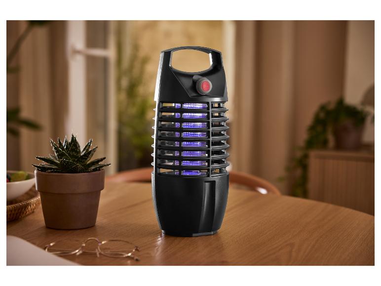 Lampe anti-moustiques électrique noire sur une table en bois avec une plante.