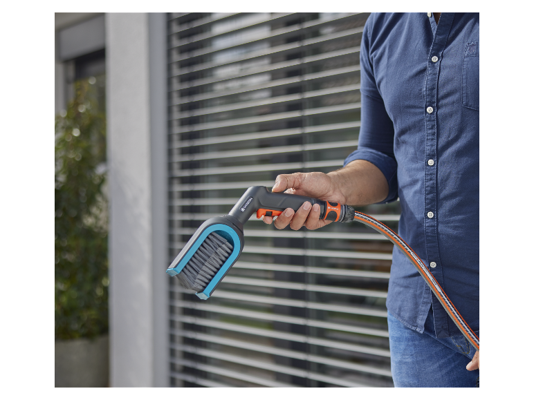 Un homme tient un nettoyeur haute pression Gardena avec une brosse et un tuyau.