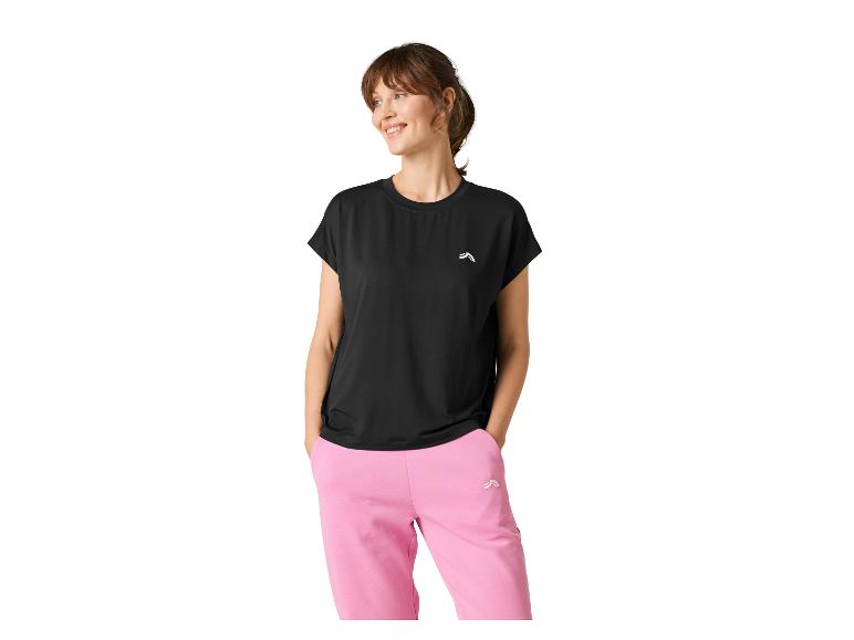 Femme en haut noir à manches courtes et pantalon de survêtement rose, souriante et regardant à droite.