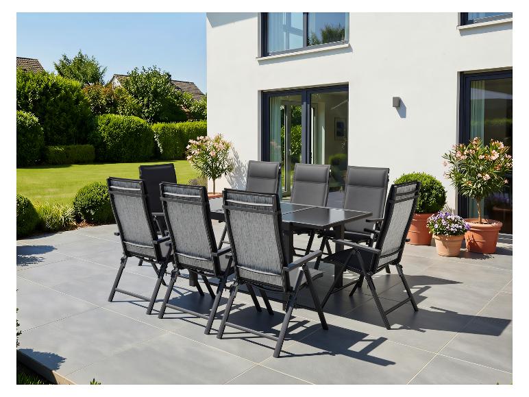 Ensemble de mobilier de jardin: table et chaises sur la terrasse, entourés de verdure et maison.