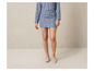 Une femme porte une jupe en tweed bleue et une veste assortie avec des escarpins beiges.