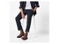 Homme en chemise noire, pantalon foncé et bottines Chelsea marron assis sur un tabouret blanc.