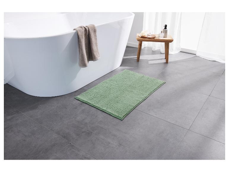 Un tapis de bain vert dans une salle de bain avec une baignoire blanche.