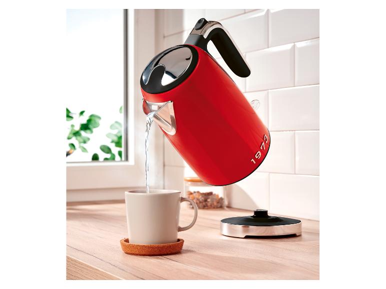 Bouilloire électrique rouge avec l'inscription «1973» versant de l'eau dans une tasse sur un comptoir en bois.