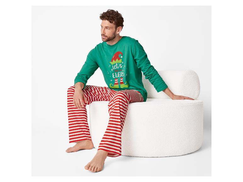 Homme assis sur une chaise blanche en pyjama de Noël vert avec l'inscription 'let's take an Elfie' et un pantalon rayé rouge et blanc.