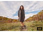Femme portant un long gilet gris, une robe marron et des bottes dans un paysage d'automne.