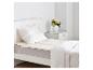 Lit en bois blanc avec un surmatelas en peau de mouton et une couette blanche.