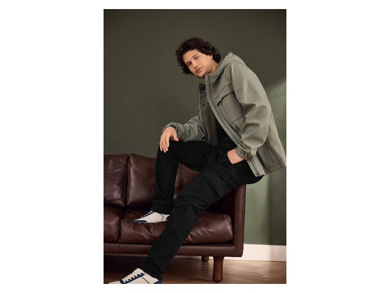 Homme en veste vert-gris, pantalon noir et baskets blanches et bleues.