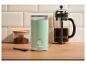 Moulin à café vert menthe, cafetière à piston et pot de café moulu sur une table en bois.
