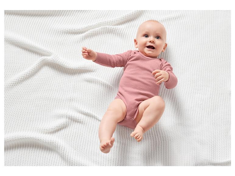Un bébé dans une combinaison rose sur une couverture blanche