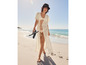 Une femme marche sur la plage avec une robe de plage blanche, un bikini et des tongs.
