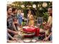 Groupe d'amis à une fête pizza DIY dans le jardin, avec four à pizza et boissons.
