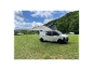 Un van Volkswagen Transporter blanc avec toit relevable et auvent déployé sur un camping.