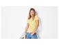Femme en t-shirt côtelé jaune et jean bleu, tenant une veste beige.
