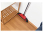 Un balai à récurer rouge avec un bord en mousse contre un sol en bois et un mur blanc.
