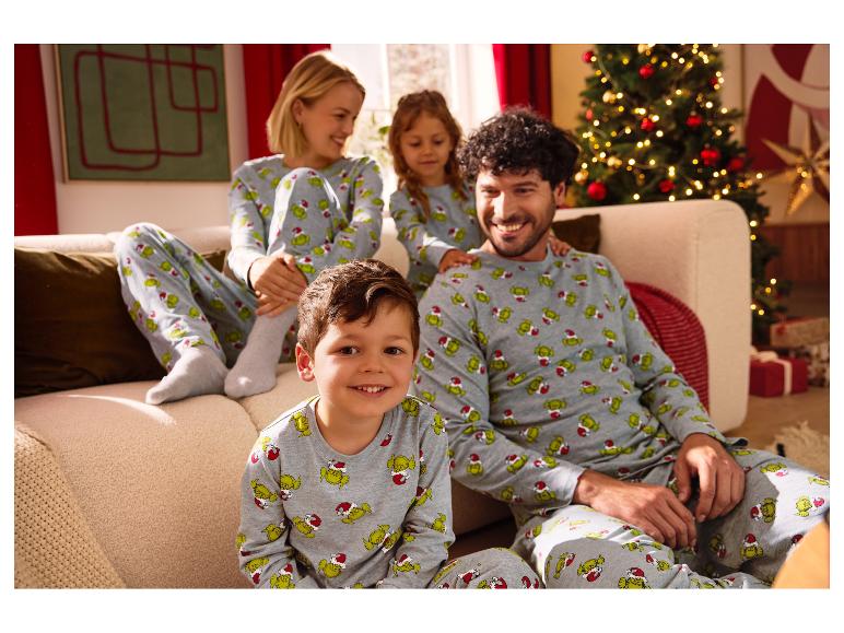 Famille portant des pyjamas Grinch assortis, assise sur un canapé près d'un sapin de Noël.