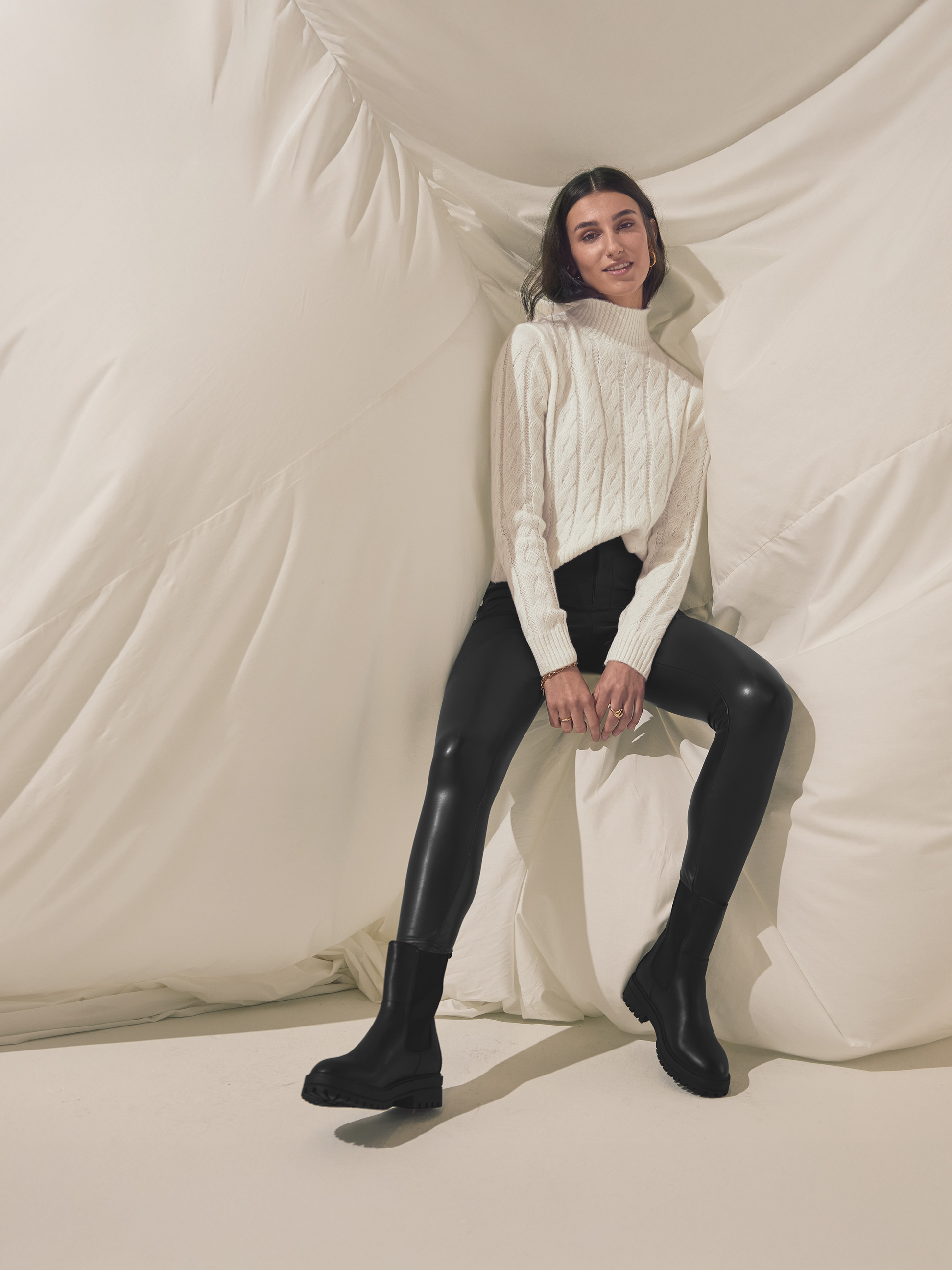 Femme en pull torsadé blanc, legging en similicuir noir et bottes noires.