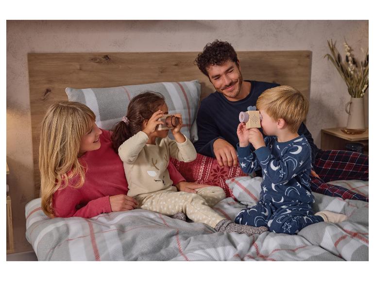 Une famille en pyjama sur un lit, avec des enfants jouant avec des appareils photo jouets.