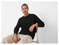 Un homme portant un pull noir et un pantalon beige.