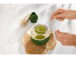 Une personne tamisant de la poudre de matcha vert dans un bol sur un support en bois.