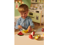 Jeune enfant jouant avec des fruits jouets et une planche à découper dans une cuisine ludique.