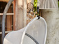 Un fauteuil suspendu en maille blanc, suspendu dans un jardin.